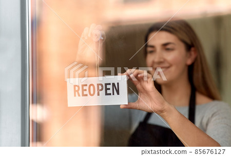 happy woman hanging reopen banner on door glass happy woman hanging reopen banner on door glass 85676127