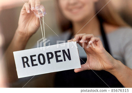 happy woman hanging reopen banner on door glass happy woman hanging reopen banner on door glass 85676315