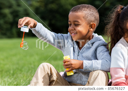happy children blowing soap bubbles at park happy children blowing soap bubbles at park 85676327