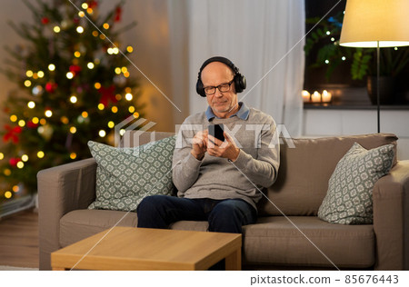senior man with smartphone and headphones at home senior man with smartphone and headphones at home 85676443