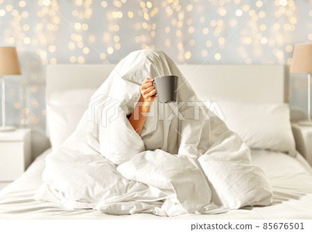 woman with coffee sitting under blanket in bed 85676501