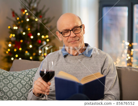 senior man drinks wine and reads book on christmas senior man drinks wine and reads book on christmas 85676552