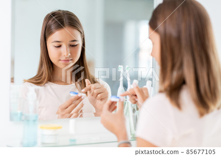teenage girl applying contact lenses at bathroom 85677105