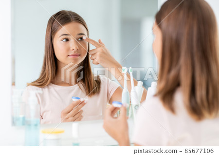 teenage girl applying contact lenses at bathroom teenage girl applying contact lenses at bathroom 85677106
