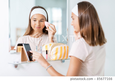 teenage girl with smartphone using make up sponge teenage girl with smartphone using make up sponge 85677108