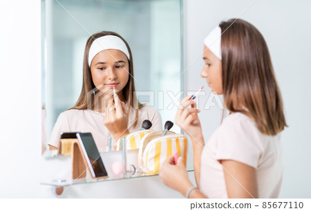 teenage girl applying lip gloss at bathroom teenage girl applying lip gloss at bathroom 85677110