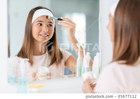 teenage girl applying face mask at bathroom teenage girl applying face mask at bathroom 85677112
