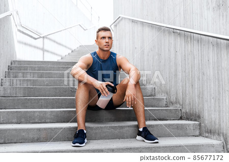 sportsman with shake in bottle sitting on stairs 85677172