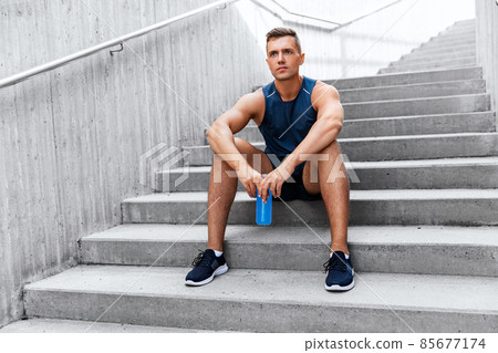 tired sportsman with bottle sitting on stairs 85677174