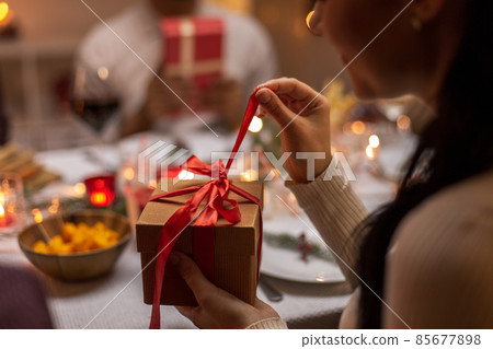 happy woman opening christmas gift at dinner party happy woman opening christmas gift at dinner party 85677898