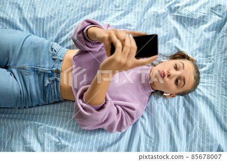 girl in earphones with smartphone lying on bed girl in earphones with smartphone lying on bed 85678007