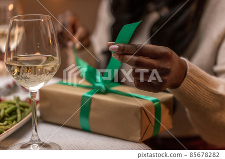 woman opening christmas gift at dinner party woman opening christmas gift at dinner party 85678282