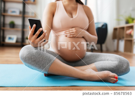 close up of pregnant woman with phone on yoga mat 85678563