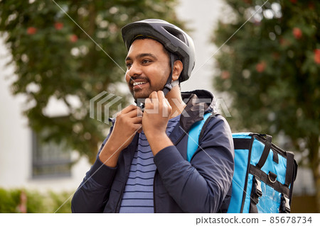 food delivery man fastening bicycle helmet in city 85678734