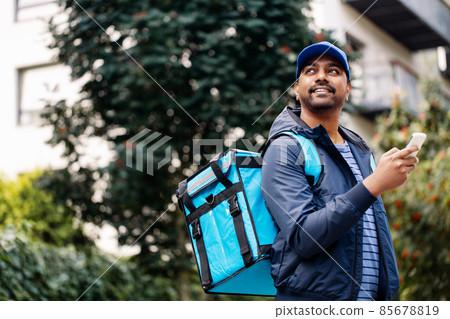 smiling indian delivery man with bag and phone smiling indian delivery man with bag and phone 85678819