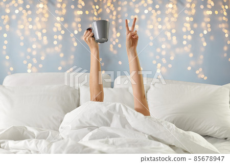 woman with coffee lying in bed showing peace woman with coffee lying in bed showing peace 85678947