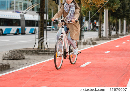 woman riding bicycle along red bike lane in city woman riding bicycle along red bike lane in city 85679007