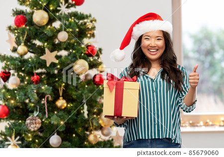 happy woman with christmas gift showing thumbs up 85679060
