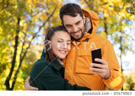 couple with smartphone over autumn park background couple with smartphone over autumn park background 85679063