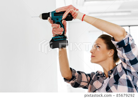 woman with perforator drilling wall at home woman with perforator drilling wall at home 85679292