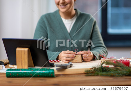 happy woman with tablet pc packing christmas gift 85679407