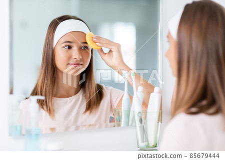 teenage girl cleaning face with sponge at bathroom teenage girl cleaning face with sponge at bathroom 85679444