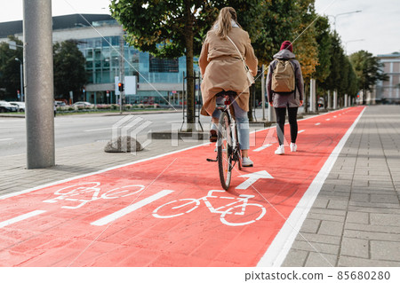 woman cycling behind pedestrian along bike lane 85680280
