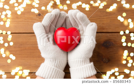 hands in white woollen gloves holding red heart 85680343