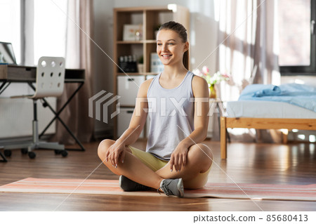 smiling teenage girl sitting on yoga mat at home smiling teenage girl sitting on yoga mat at home 85680413