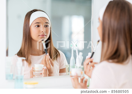 teenage girl applying face mask at bathroom 85680505