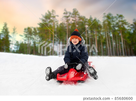 happy boy sliding on sled down snow hill in winter 85680600