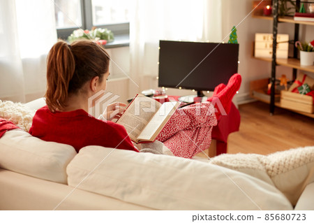 young woman reading book at home on christmas 85680723