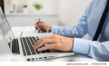 Working Man Conept The male officer sitting in the office, laying his left hand on the laptop, and writing something on the paper with his right hand Working Man Conept The male officer sitting in the office, laying his left hand on the laptop, and writing something on the paper with his right hand 85683546