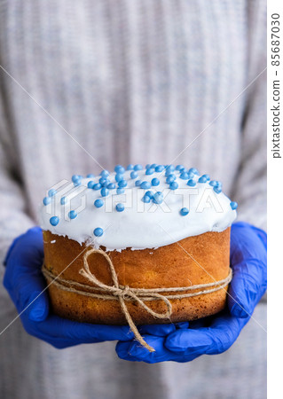 Hands in blue gloves hold Easter cake with white topping and blue sprinkles. Woman holding traditional Russian Easter cake. Homemade pie for spring holiday celebration 85687030