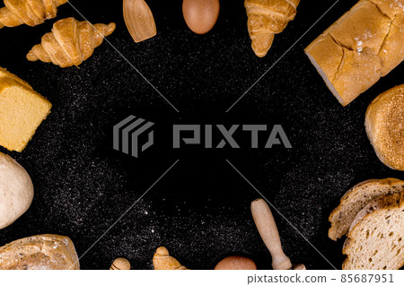 bread concept slices of bread, buns, croissants, and loaves of bread arranged in circle on the black scene and sprinkling flour dust on it 85687951