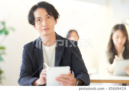 A young man sitting in a classroom and taking notes on a tablet 85689419