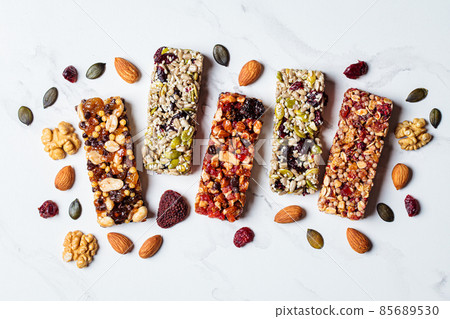 Energy granola bars with different seeds, nuts and dried fruits and berries on white marble background. Healthy snack concept. Energy granola bars with different seeds, nuts and dried fruits and berries on white marble background. Healthy snack concept. 85689530