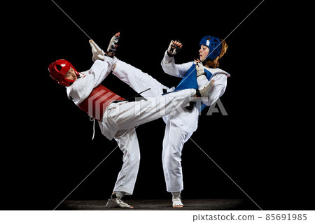 Dynamic portrait of two young women, taekwondo athletes training together isolated over dark background. Concept of sport, skills Dynamic portrait of two young women, taekwondo athletes training together isolated over dark background. Concept of sport, skills 85691985