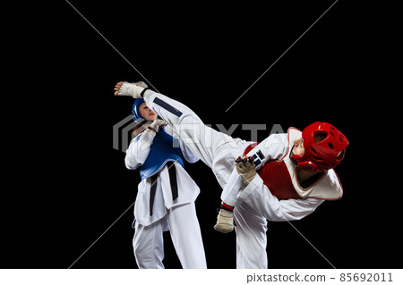 Dynamic portrait of two young women, taekwondo athletes training together isolated over dark background. Concept of sport, skills 85692011