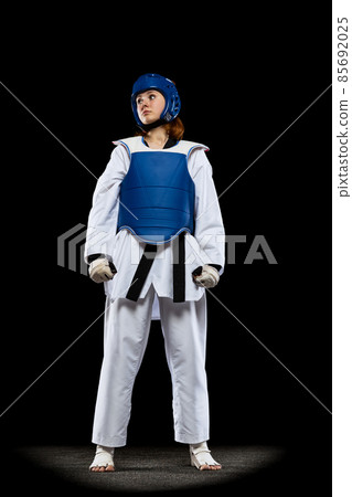 Portrait of young girl, taekwondo practitioner posing isolated over dark background. Concept of sport, skills Portrait of young girl, taekwondo practitioner posing isolated over dark background. Concept of sport, skills 85692025