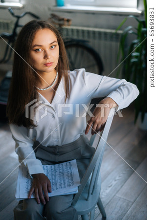 Vertical portrait of successful young woman pianist holding in hands score with musical notes in dark classroom, looking at camera. Vertical portrait of successful young woman pianist holding in hands score with musical notes in dark classroom, looking at camera. 85693831