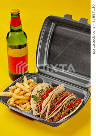 Birria tacos in takeaway container with fries and bottle of drink on yellow background Birria tacos in takeaway container with fries and bottle of drink on yellow background 85697130
