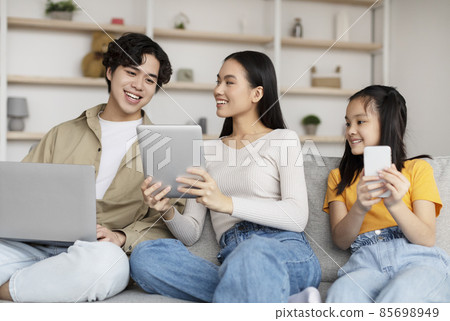 Happy korean millennial woman showing to husband and teen daughter video, advertisement and offer on tablet Happy korean millennial woman showing to husband and teen daughter video, advertisement and offer on tablet 85698949
