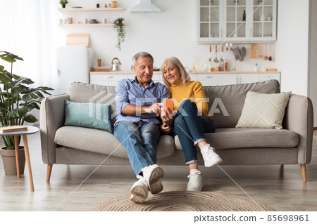 Happy Mature Husband And Wife Using Smartphone Sitting At Home 85698961