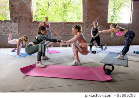 Young fit Women on a Yoga Pilates crossfit group class in gym. They stretch, stay in asana poses in 85699298