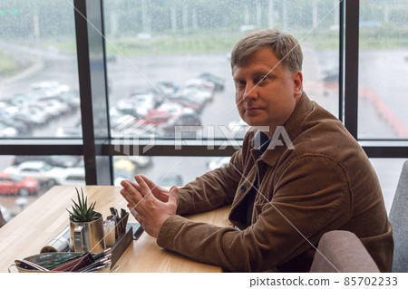 Portrait of an adult man in a corduroy jacket waiting for his order at a table in a cafe Portrait of an adult man in a corduroy jacket waiting for his order at a table in a cafe 85702233