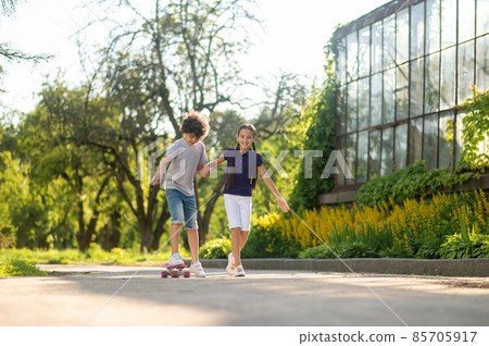 Cheerful girl teaching a boy to skateboard Cheerful girl teaching a boy to skateboard 85705917
