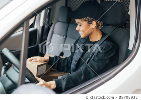 Smiling woman courier sitting on a driver seat checking boxes for delivery Smiling woman courier sitting on a driver seat checking boxes for delivery 85705938