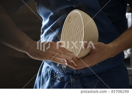 Male baker lightly flouring proofing basket for home made sourdough bread. Male baker lightly flouring proofing basket for home made sourdough bread. 85706299