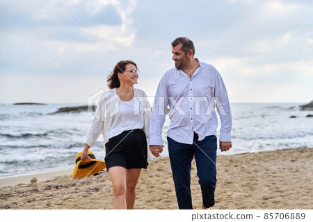 Happy middle-aged couple walking together on the beach. Happy middle-aged couple walking together on the beach. 85706889